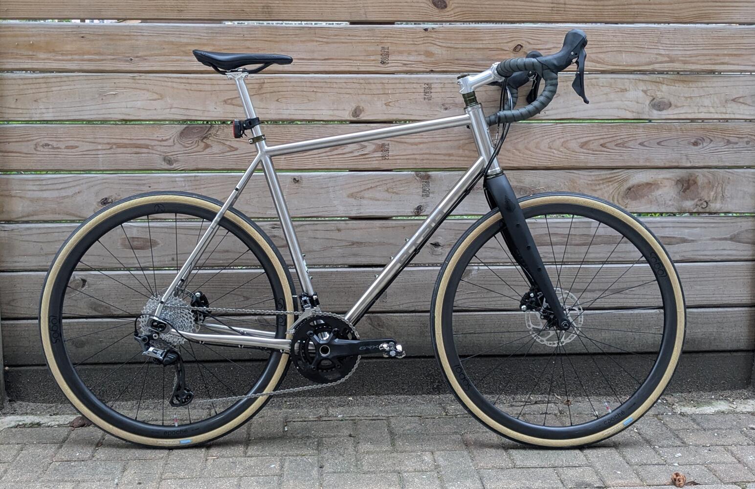 An unpainted steel road bike, leaning against a wood fence.