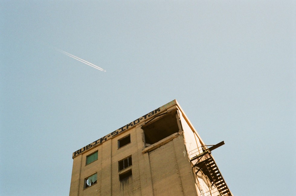 a plane flying high over an large, abandoned, crumbling building